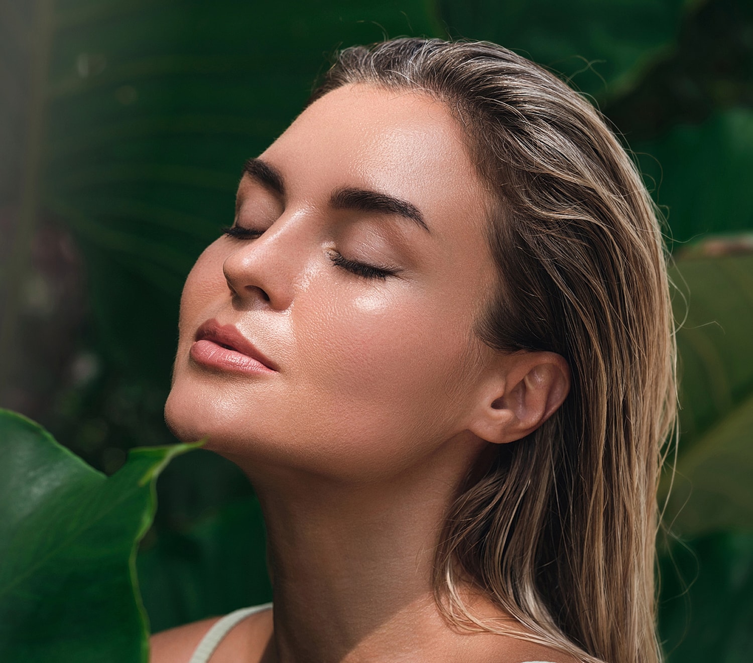 Woman with closed eyes amidst lush greenery.