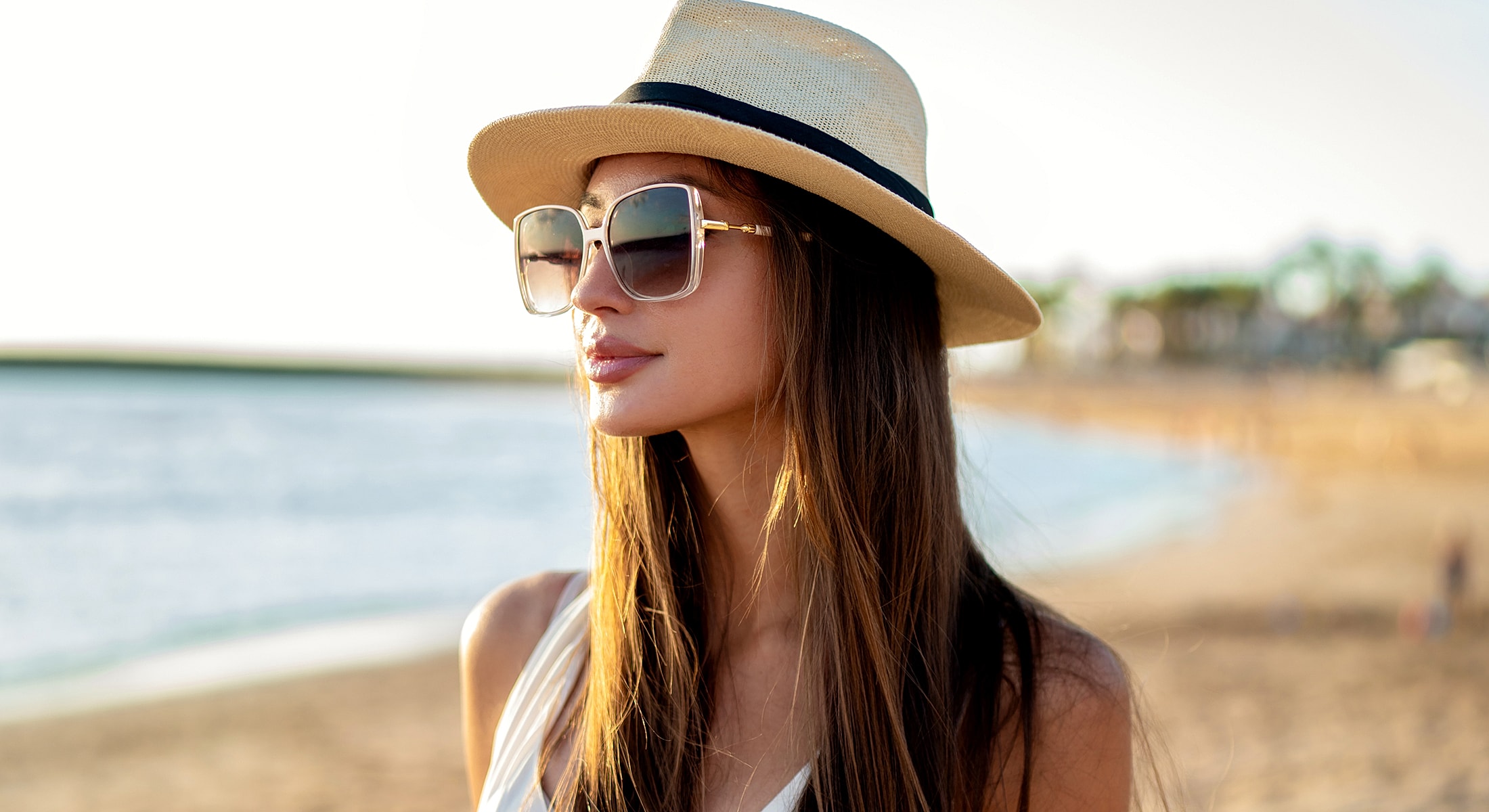 Woman in hat and sunglasses by the beach.